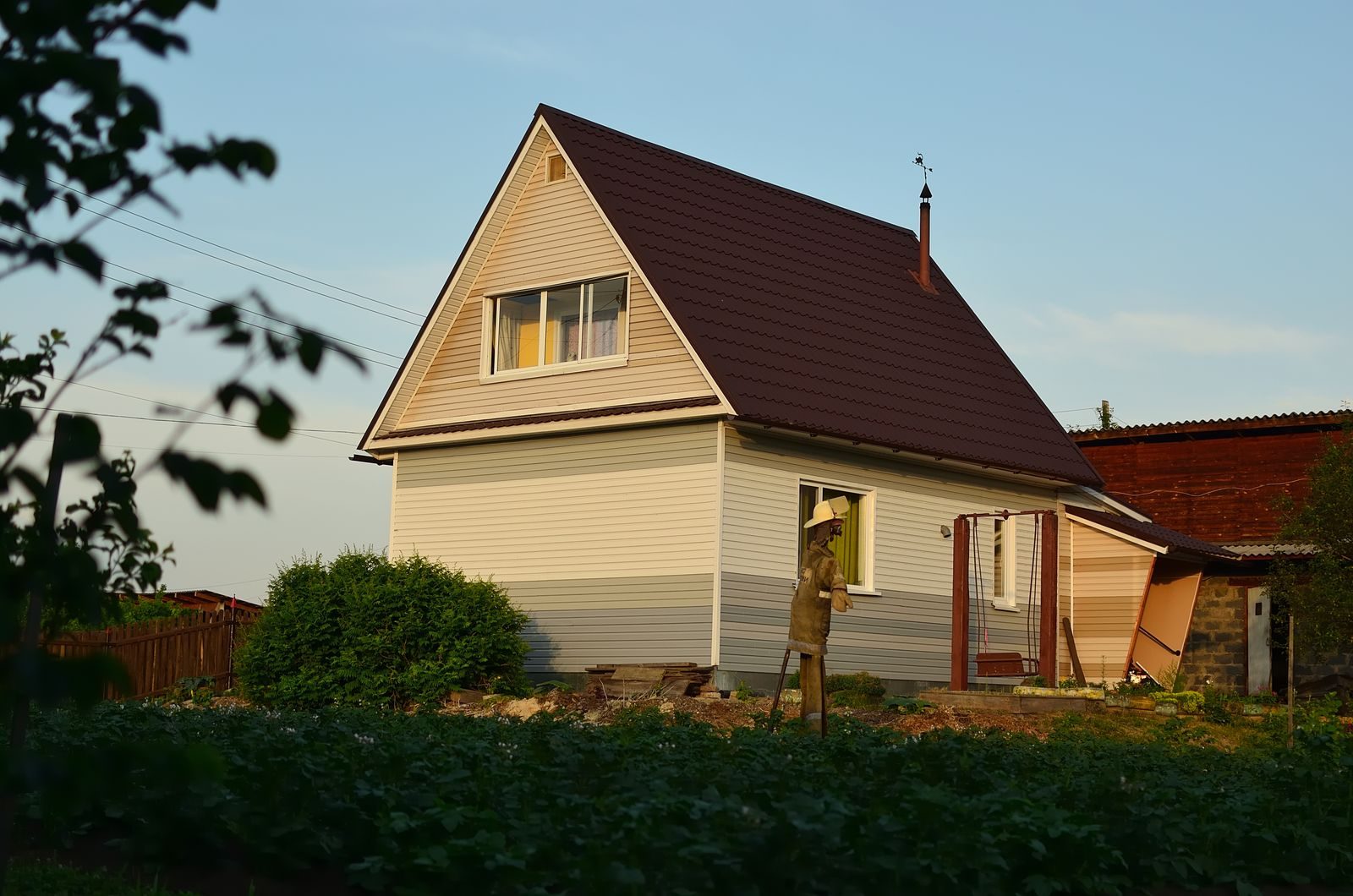 A suburban house with garden and scarecrow under warm evening sunlight, showcasing rustic charm.